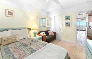 Ein Schlafzimmer mit Bett, Nachttisch, Lampe, einer Couch und Blick auf den Balkon.
