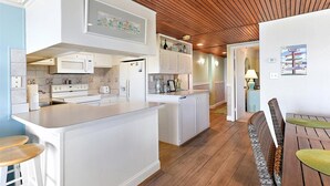 A modern kitchen with white cabinetry, a central island, and a wooden ceiling.