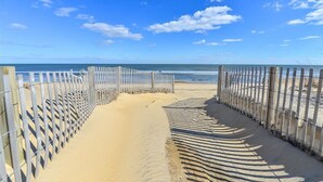 A beach pathway with a wooden fence on both sides leading to the ocean.