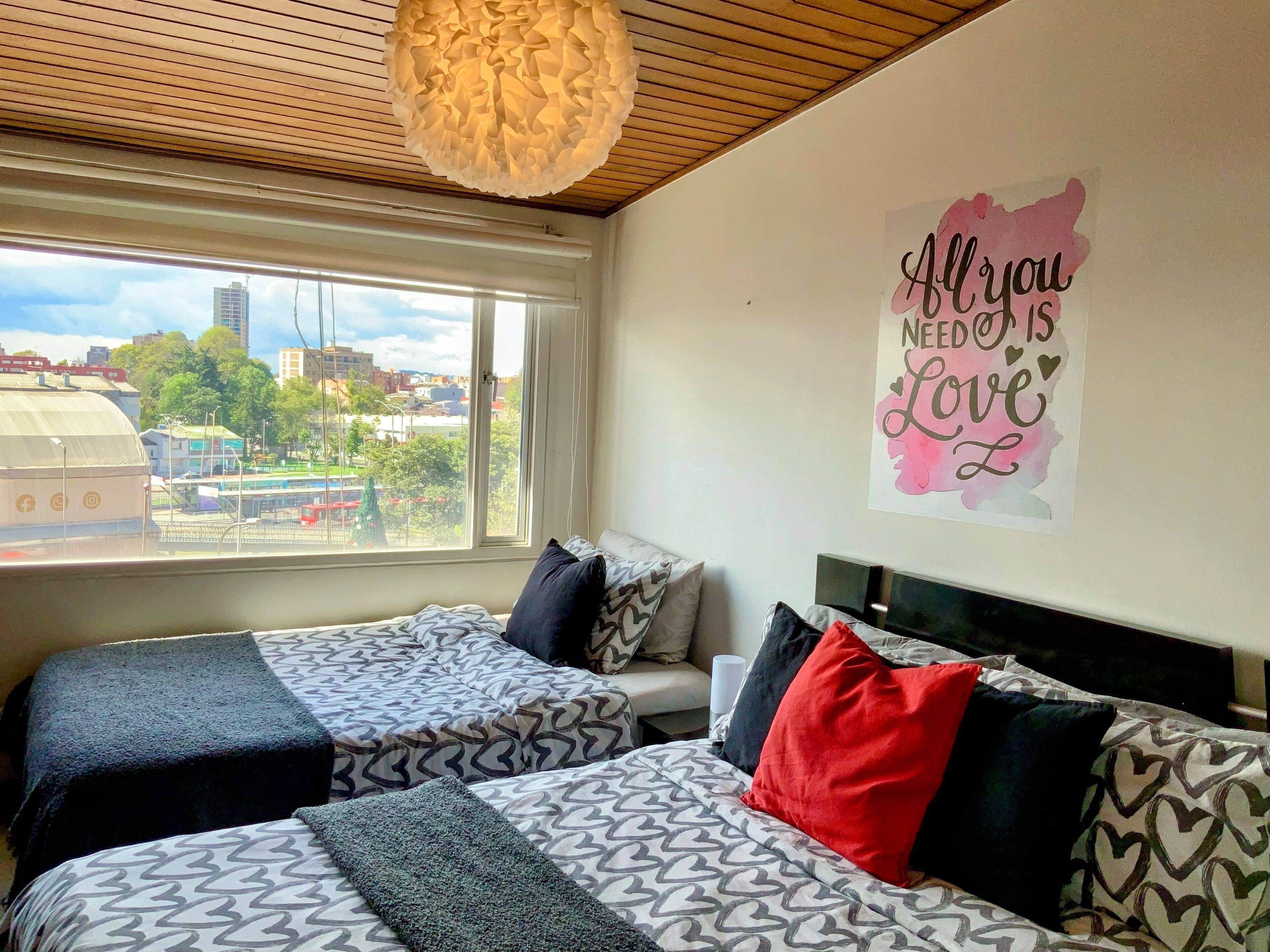 A hotel room with two beds, a large window with a city view, a ceiling light fixture, and a motivational poster on the wall.