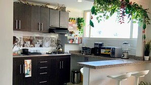 A modern kitchen with dark cabinets, a central island with bar stools, a window with hanging plants, and a tiled backsplash. - 3 Level Luxe Penthouse • 7 Real Beds • Mountain Views & Balcony • Zona T (Bogota)