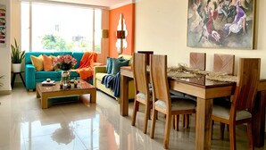A living room with a teal sofa, a wooden dining table, and a large painting on the wall. - 3 Level Luxe Penthouse • 7 Real Beds • Mountain Views & Balcony • Zona T (Bogota)