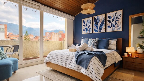 A bedroom with a large bed, a view of the city through large windows, and artwork on the wall. - 3 Level Luxe Penthouse • 7 Real Beds • Mountain Views & Balcony • Zona T (Bogota)