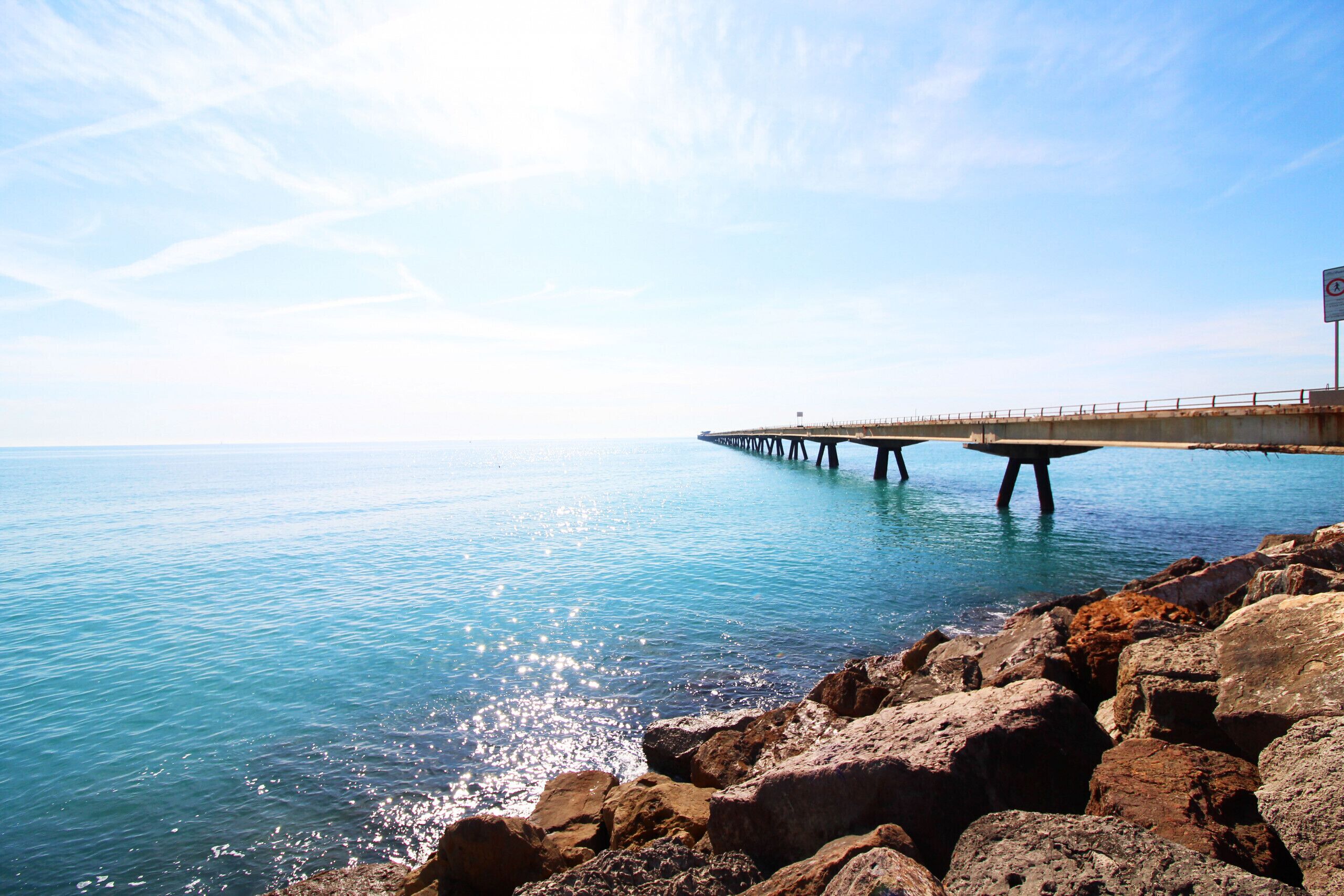 Un muelle que se adentra en aguas tranquilas, con una costa rocosa en primer plano.