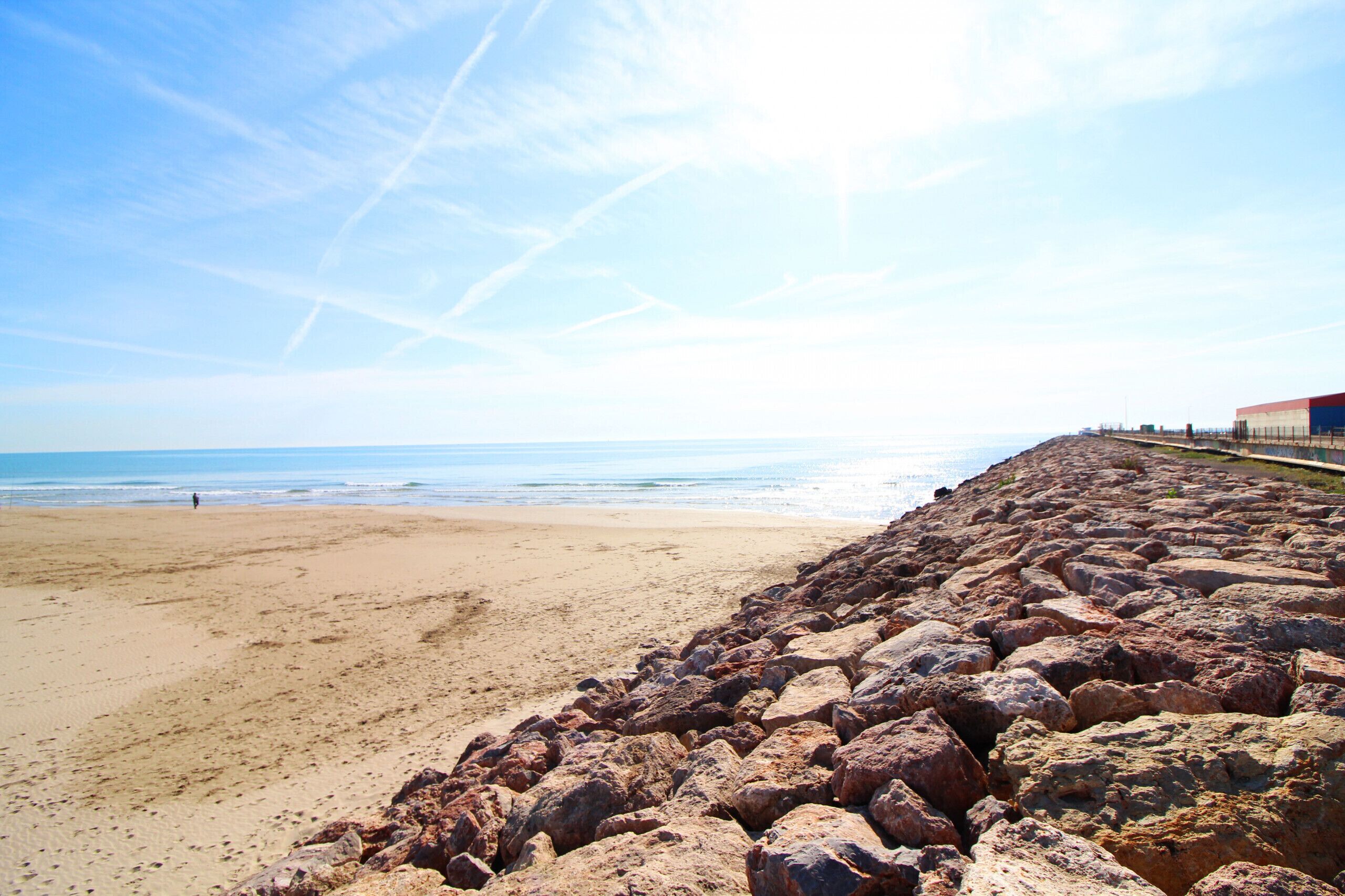 A beach with a rocky breakwater and a clear sky.