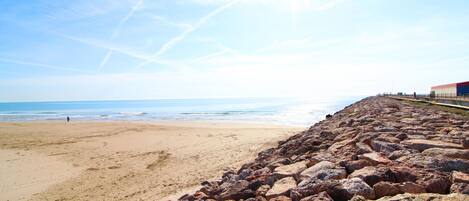 A beach with a rocky breakwater and a clear sky.