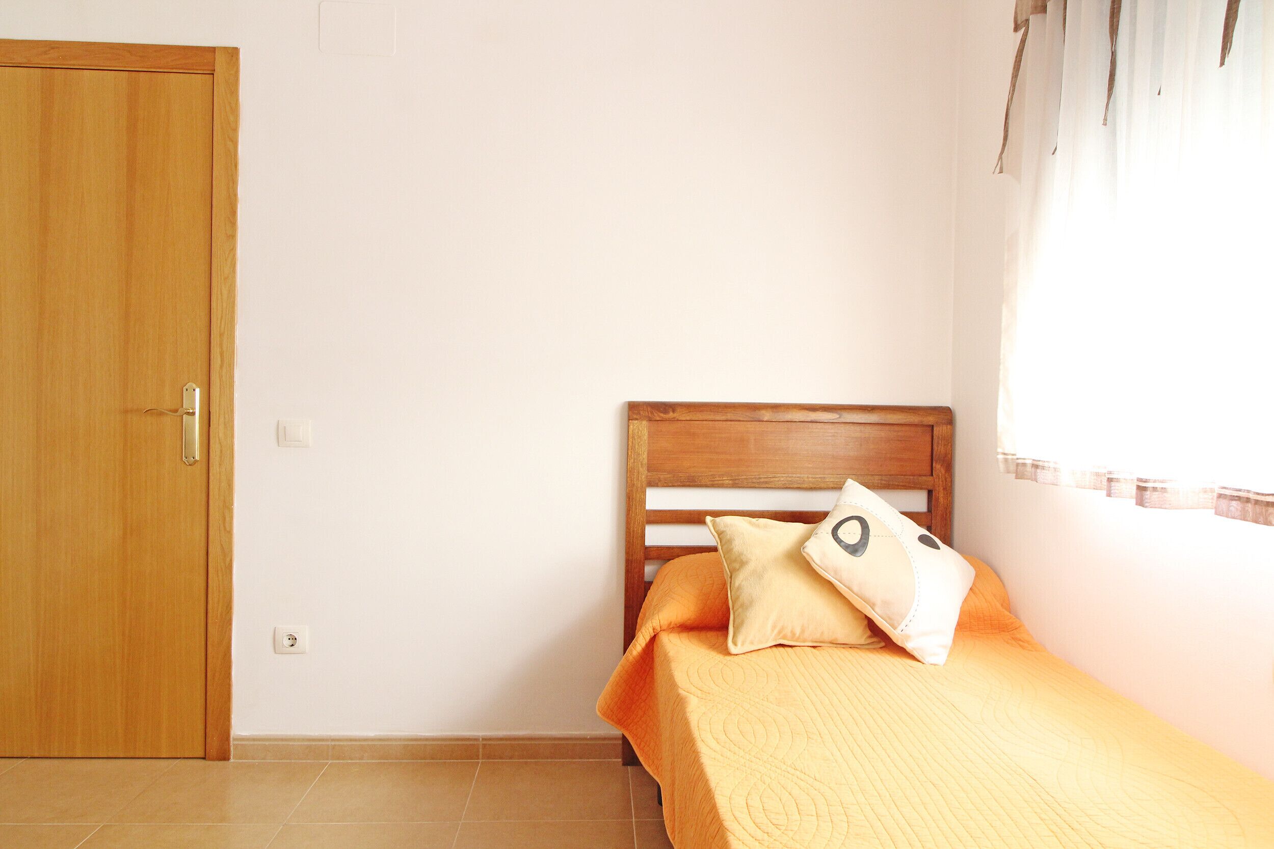 Un dormitorio con una puerta de madera, una cama con colcha naranja y una ventana con cortinas.