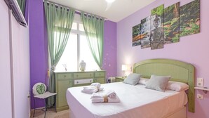 Ein Schlafzimmer mit einem Bett, grünen Vorhängen, einem Schreibtisch, einem Stuhl und einer Wand mit drei Bildern.