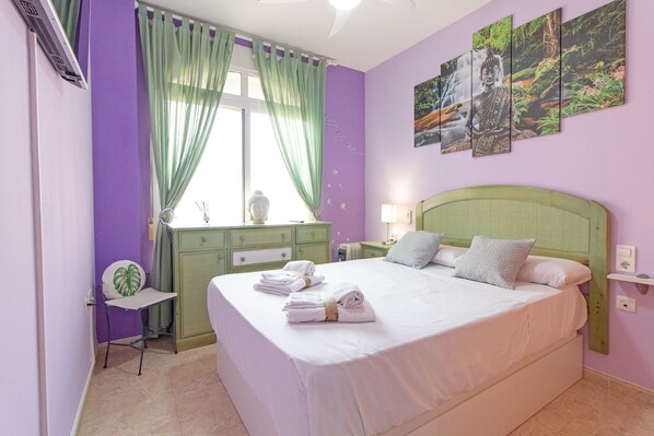 A bedroom with a bed, green curtains, a desk, a chair, and a wall with three paintings.