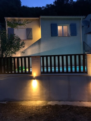 Une maison à deux étages avec une piscine, une clôture et un éclairage extérieur.