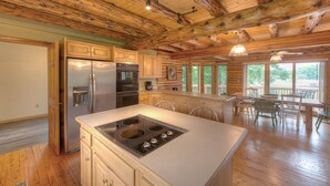 Une cuisine spacieuse avec des poutres en bois, un grand îlot central doté d’une plaque de cuisson et un coin repas avec des chaises et une table.