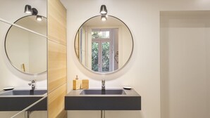 Een badkamer met een ronde spiegel, twee wasbakken en een raam.