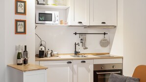 Een compacte keuken met witte kastjes, een magnetron, een spoelbak en een klein aanrecht.
