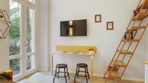 Een kamer met een houten bureau, twee zwarte krukken, een aan de muur bevestigde televisie en een houten ladder.