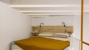 Een slaapkamer met een bed, hoofdeinde, nachtkastje en een wandlamp.