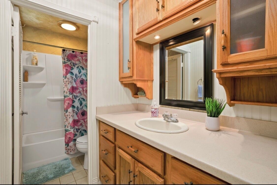 A bathroom with wooden cabinets, a white sink, a mirror, and a shower curtain with floral patterns.