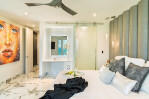 Moderni hotellihuone, jossa on suuri sänky, peilillä varustettu kylpyhuone ja kattotuuletin.