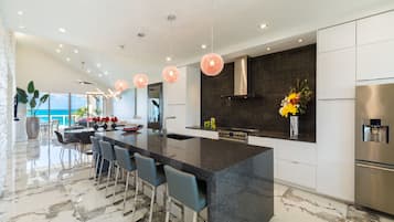 A modern kitchen with a large island, bar stools, stainless steel appliances, and pendant lighting.