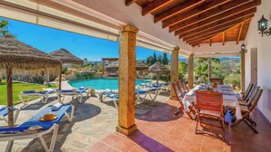 A poolside area with lounge chairs and a dining table, overlooking a swimming pool and a scenic landscape.