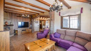 A spacious living room with a large flat-screen TV, wooden furniture, and a stone fireplace. - Villa Biznaga Mijas by Ruralidays (Málaga)