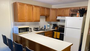 A kitchen with wooden cabinets, a white refrigerator, a microwave, a stove, and a sink. There are two bar stools and a coffee maker on the counter.