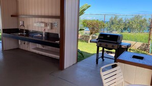An outdoor kitchen with a sink, a grill, and a table with a chair.