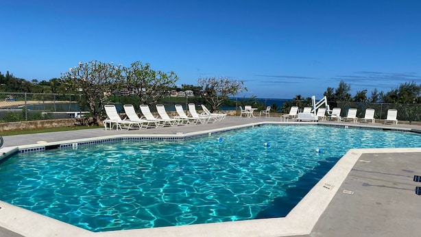 A swimming pool with clear blue water, surrounded by white lounge chairs and a view of the ocean.