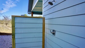 A wooden door with a metal handle, a metal doorbell, and a metal showerhead on a light blue siding house.