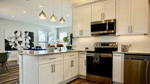 A modern kitchen with white cabinets, stainless steel appliances, a large island, and pendant lighting.