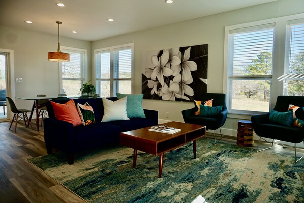 Una sala de estar moderna con un sofá azul oscuro, dos sillones, una mesa de centro de madera y una gran obra de arte floral en la pared.
