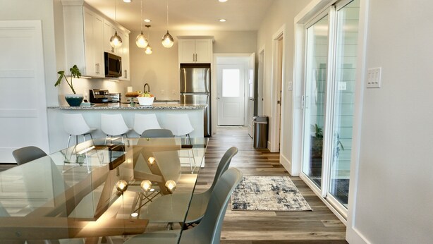 A modern kitchen with white cabinets, stainless steel appliances, and a glass dining table with chairs.