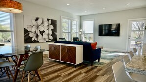 A modern kitchen with a wooden floor, a dining area with chairs, a large cabinet, and a TV mounted on the wall.