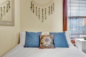 A bed with white and blue bedding, a decorative pillow, and a wall with hanging ornaments.
