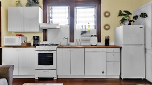Una cocina compacta con gabinetes blancos, estufa, microondas y refrigerador.