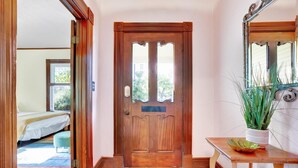 Una puerta de madera con un panel de vidrio, una mesita con una planta en maceta y una cama en la habitación contigua.