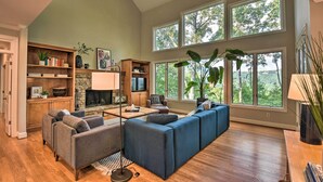 A spacious living room with a large sectional sofa, a fireplace, and multiple windows offering a view of the outdoors. - Luxe Big Canoe Resort Home w/ 3 Decks & Mtn Views! (Jasper)