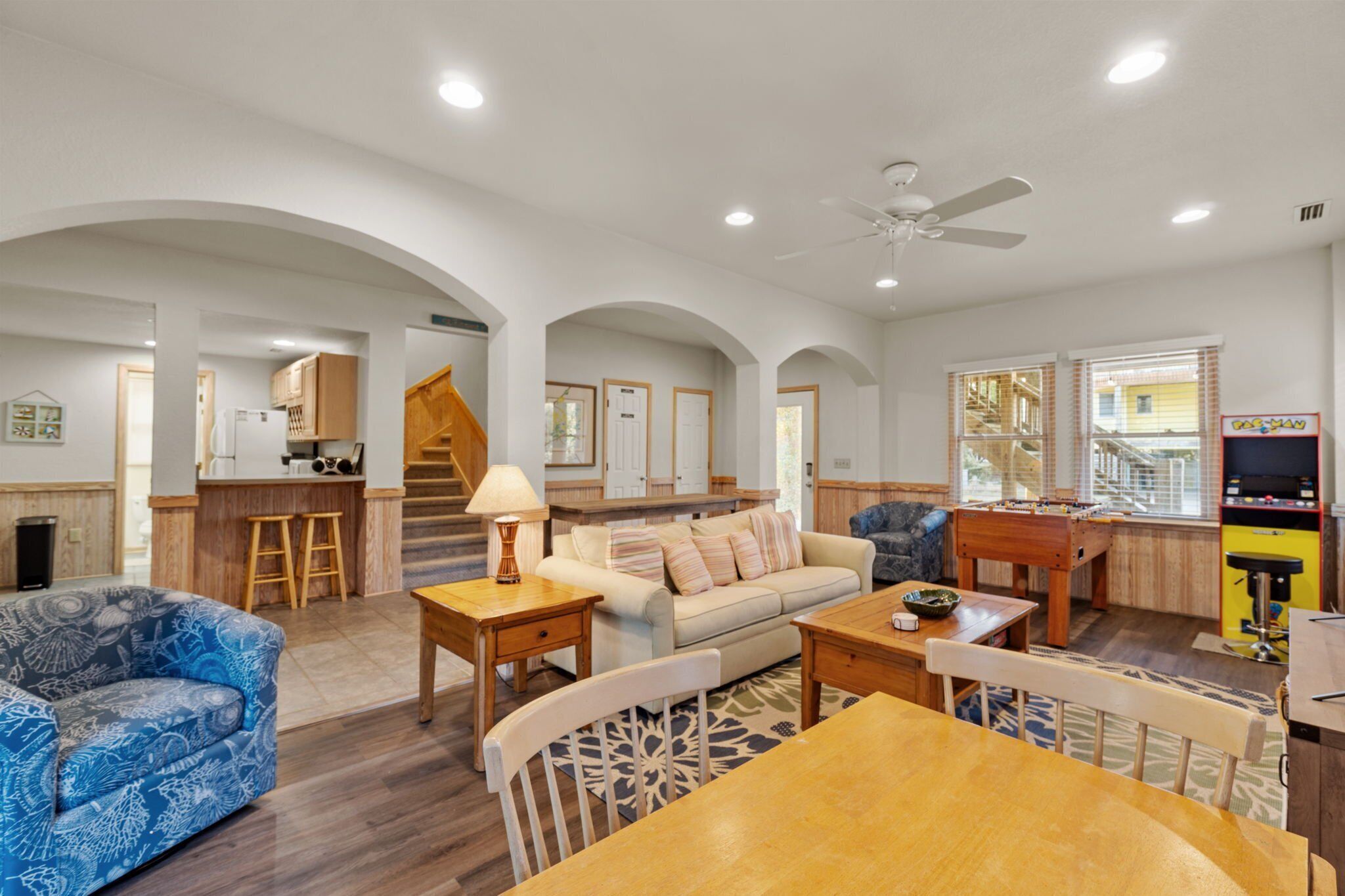 A spacious living area with a sofa, coffee table, and a dining table. There is a kitchen area with a refrigerator and a bar.
