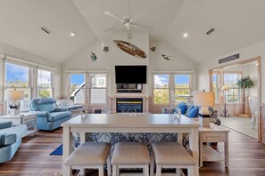 A spacious living room with a large island, a fireplace, and a ceiling fan. - 1755 - Don't Worry Beach Happy - Walk to Beach | Pool, Hot Tub & Tiki Bar (Corolla)