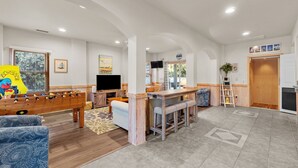 A spacious living area with a foosball table, a television, and a bar area with stools. - 1755 - Don't Worry Beach Happy - Walk to Beach | Pool, Hot Tub & Tiki Bar (Corolla)