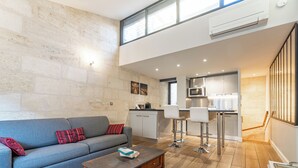 A modern living room with a grey sofa, wooden coffee table, and a kitchen area with a microwave and bar stools. - Superb quality duplex in hypercentre with rooftop and air conditioning (Bordeaux)