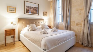 A neatly made bed with white linens and pillows, a wooden nightstand with a lamp, and a framed cityscape picture on the wall. - Superb quality duplex in hypercentre with rooftop and air conditioning (Bordeaux)