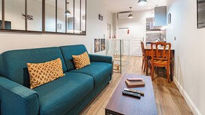 Un salon moderne avec un canapé de couleur turquoise, une table à manger en bois et une cuisine en arrière-plan.