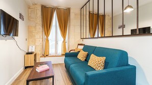 Un salon moderne avec un canapé de couleur turquoise, une table basse en bois et un téléviseur fixé au mur.