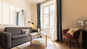 Una sala de estar moderna con un sofá gris, una mesa de centro redonda, una mesita auxiliar, una silla y un ventilador de pie.