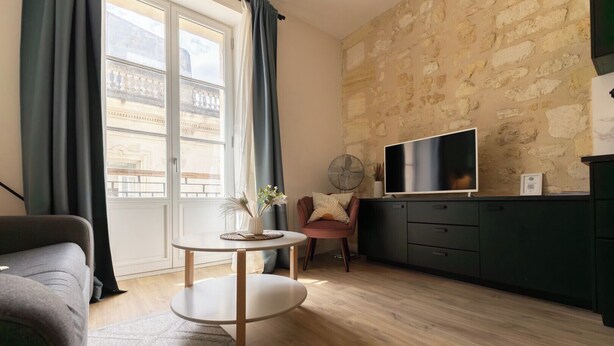 Una sala de estar moderna con una pared de piedra, una mesa redonda, un sofá, un televisor y un ventilador.