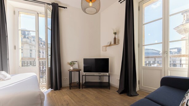 Ett hotellrum med en säng, en tv, en soffa och stora fönster med utsikt över staden.