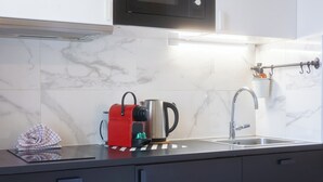 Et moderne køkken med en stålkedel, en rød elkedel, en vask og et marmorbakpanel.