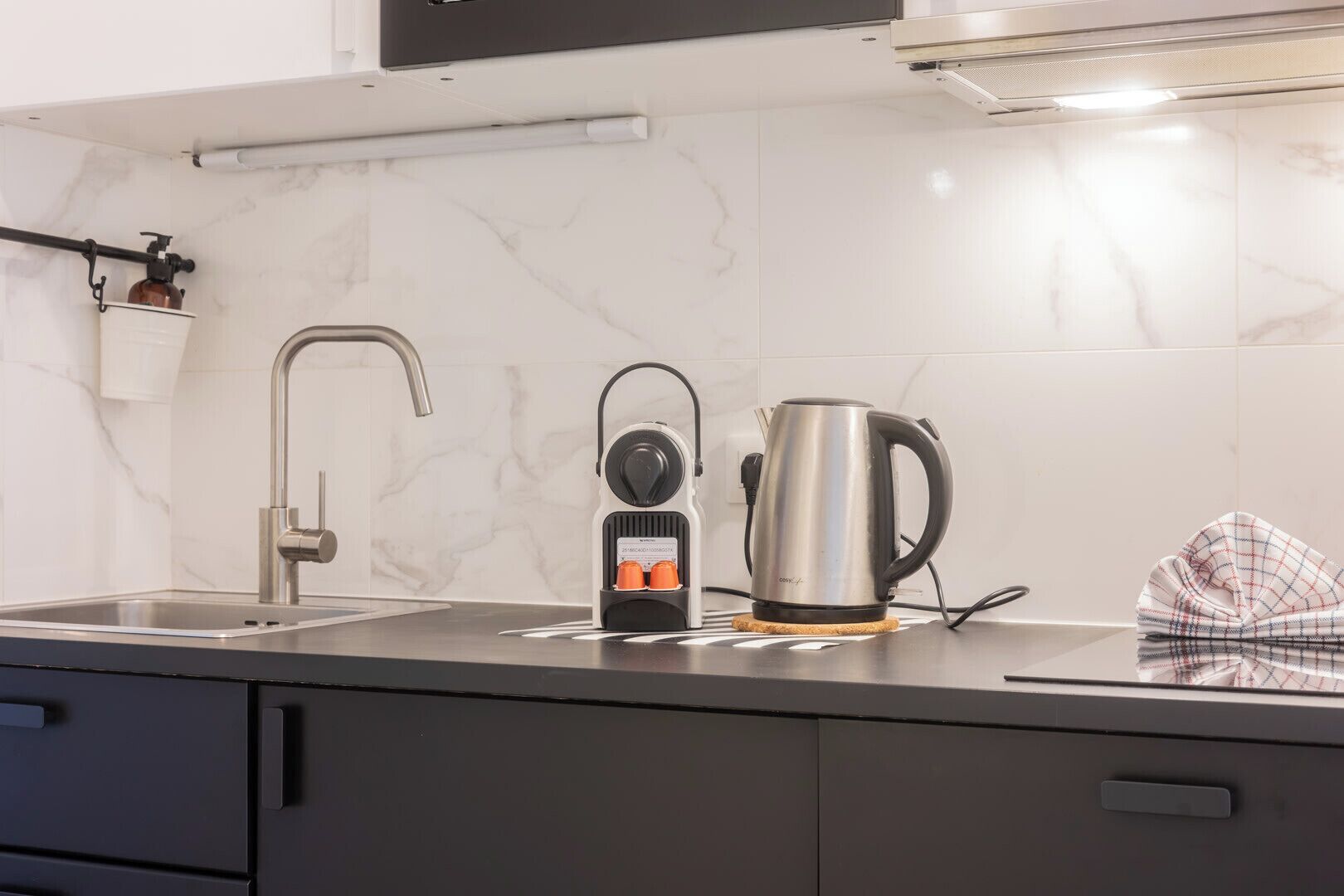 Uma cozinha com uma torneira moderna, uma chaleira e uma cafeteira sobre o balcão.