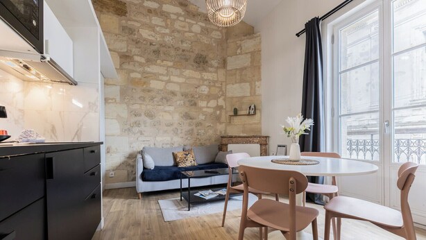 A modern kitchen with a stone wall, a dining area with a round table and chairs, and a sofa in the background.