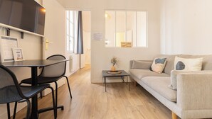 A modern living room with a sofa, a dining table with chairs, a small side table, and a window with blinds. - Beautiful renovated apartment for 2 in front of the Gare Saint-Jean (Bordeaux)